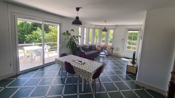 A spacious room with a dining table, chairs, a sofa, and a large window offering a view of greenery outside. - Town house on the banks of the vienne (Châtellerault)