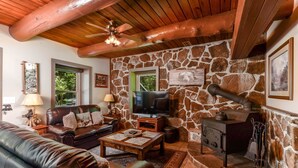 Uma sala de estar acolhedora com parede de pedra, móveis de couro, lareira e televisão.