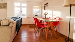 Een gezellige woonkamer met een bank, een glazen eettafel met rode stoelen en een lamp.