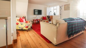 Een ruime woonkamer met een grote bank, een rood tapijt en een aan de muur bevestigde televisie.