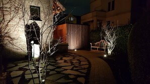 Ein nächtlicher Blick auf einen Innenhof mit einem gepflasterten Weg, einer Bank und einem Gebäude mit Backsteinfassade.
