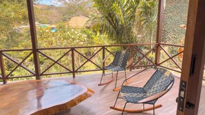 A wooden deck with two rocking chairs and a wooden table, overlooking a lush landscape with trees and hills. - Portales del Tayrona Garden Hotel (Santa Marta)