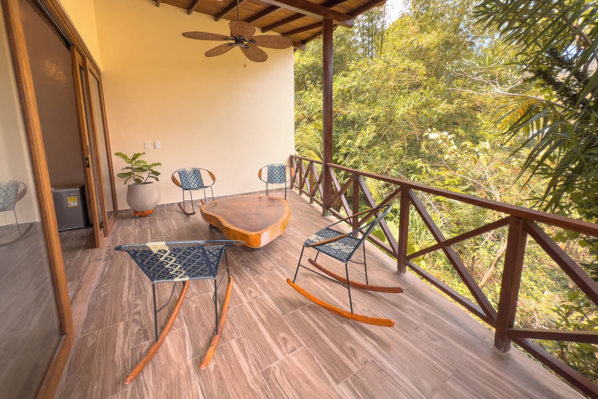 A wooden deck with a ceiling fan, a table, and two rocking chairs.