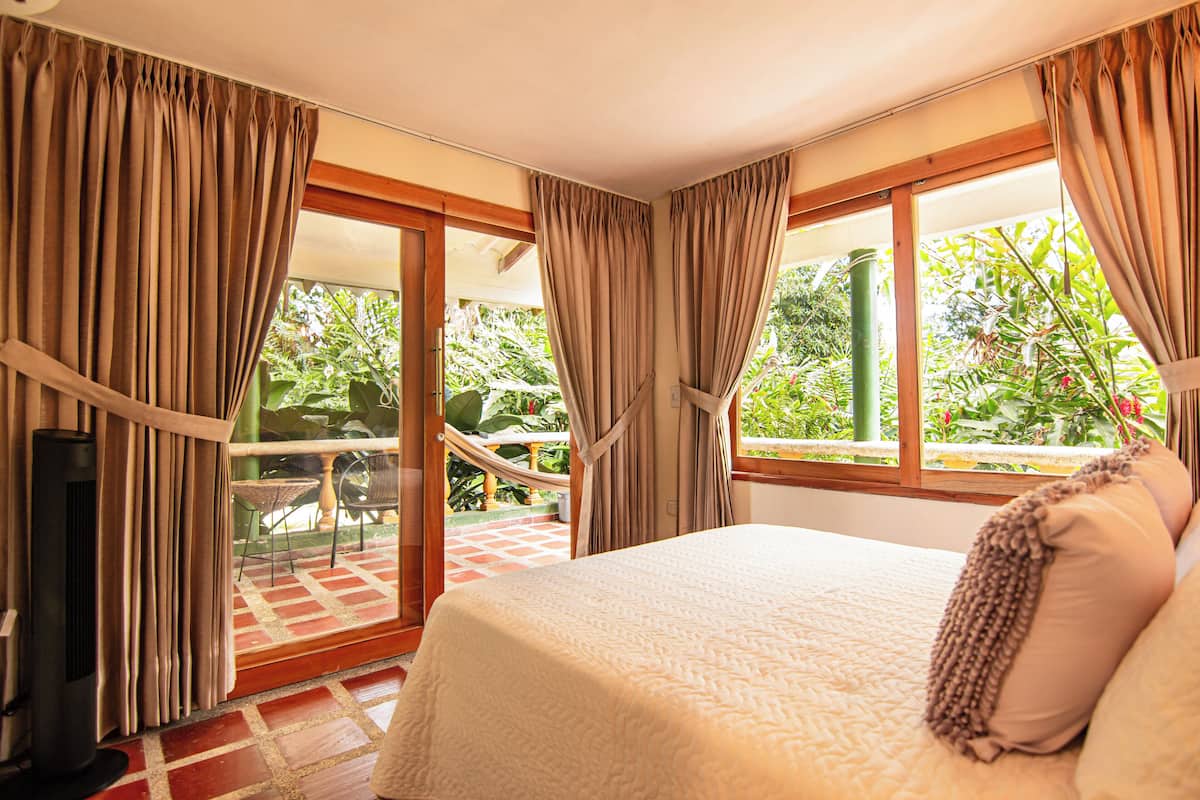 A bedroom with a bed, curtains, a TV, and a view of a garden.