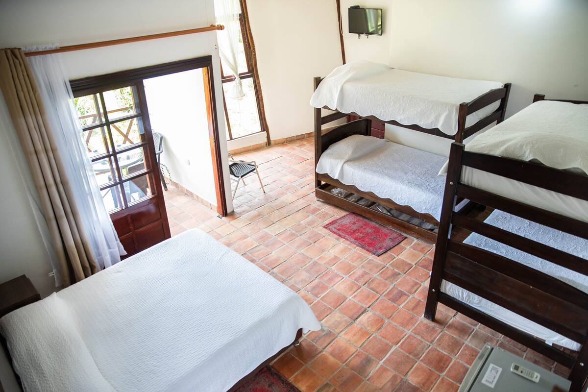 A room with a bed, a chair, a TV, and a window with curtains.