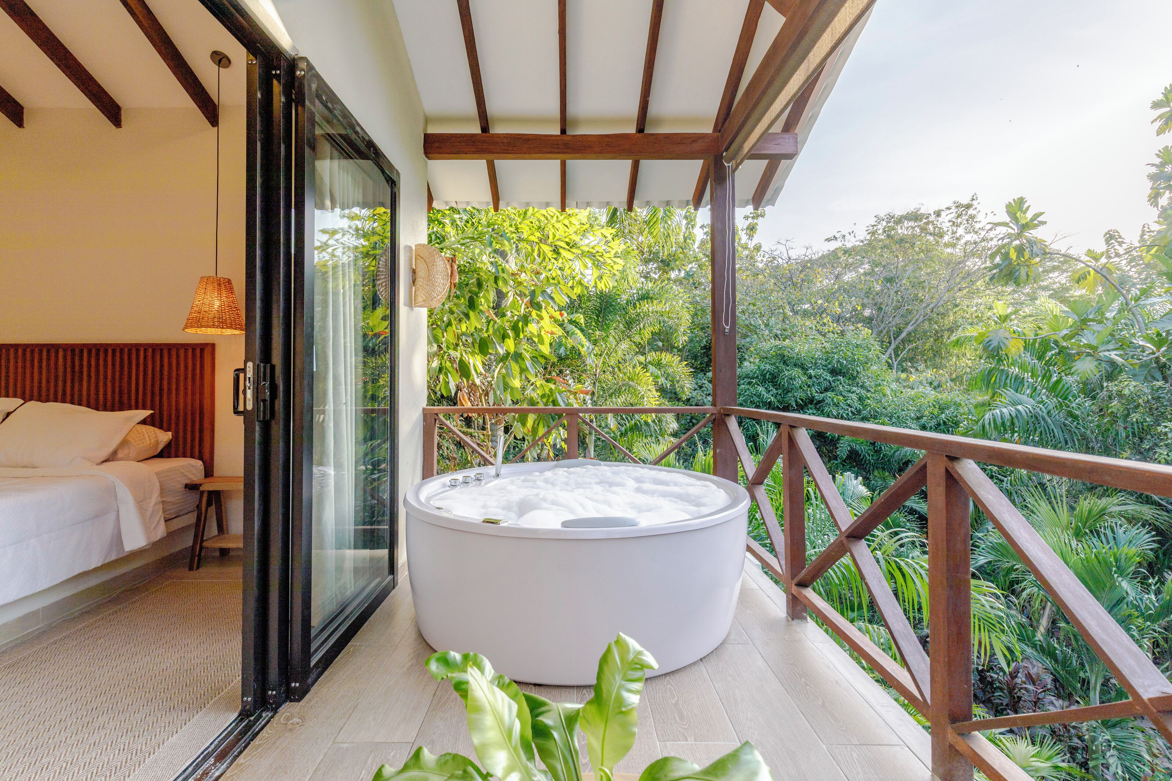 Un balcón con un jacuzzi, una cama y vistas a abundante vegetación.