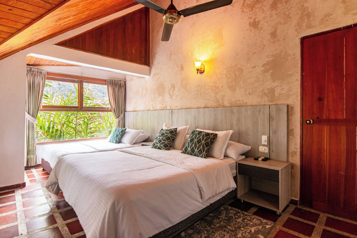 A bedroom with two beds, a ceiling fan, a nightstand, a wooden door, and a window with curtains.