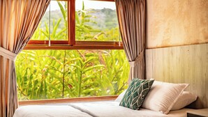 A bedroom with a large window, curtains, a bed with pillows, and a view of greenery outside. - Portales del Tayrona Garden Hotel (Santa Marta)