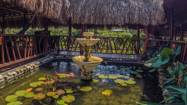 A thatched-roof structure with a central water feature surrounded by rocks and lily pads. - Portales del Tayrona Garden Hotel (Santa Marta)