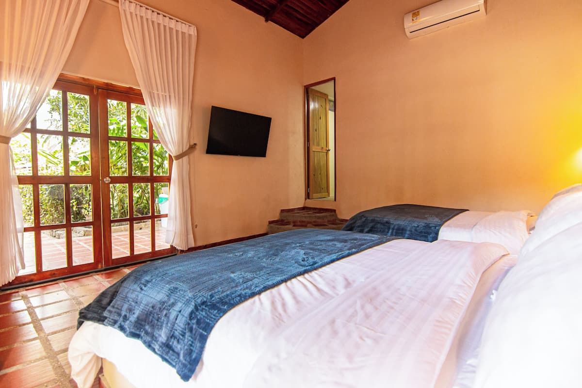 A bedroom with two beds, a TV, a mirror, and a sliding glass door leading to an outdoor area.
