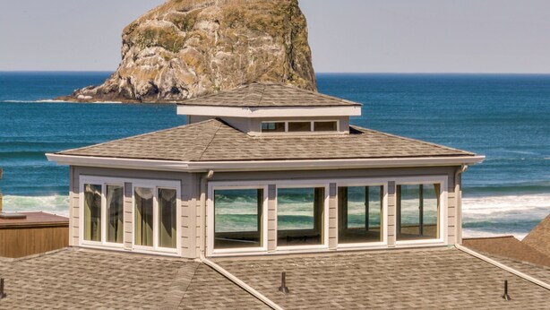 Un edificio con techo plano y ventanas amplias, con vistas a un litoral rocoso y el océano.