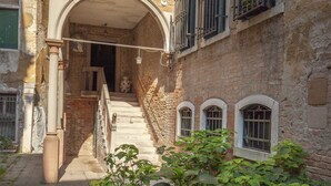 A historic building with a stone facade, a staircase leading to an upper level, and a small balcony with metal railings.
