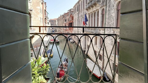 A balcony with a view of a canal, boats, and historic buildings.