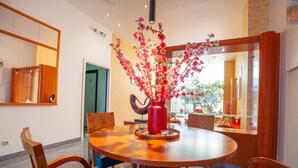 A dining area with a round wooden table, chairs, a red vase with flowers, and a mirror on the wall. - Hotel Monaco Zeebrugge Beach (Bruges)