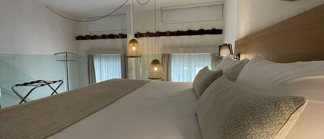 Habitación de hotel con una cama grande, cabecera de madera, lámpara colgante y vista a la ciudad por la ventana.