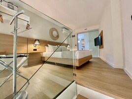 Quarto de hotel moderno com uma cama, mesas de cabeceira, um espelho e uma TV na parede.