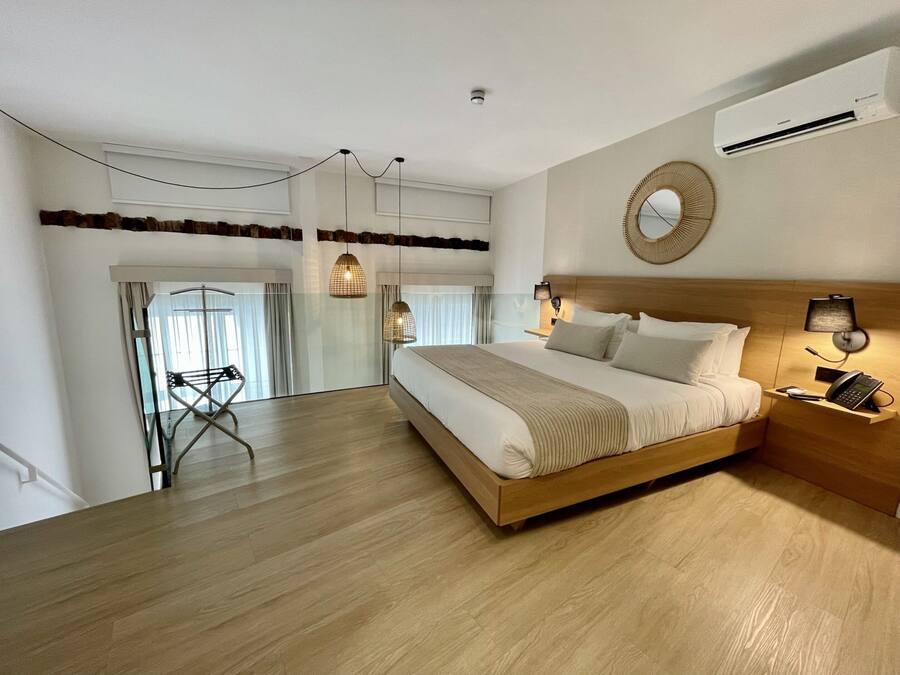 A modern hotel room with a large bed, a bedside table with a phone, a mirror, and a wall-mounted air conditioner.