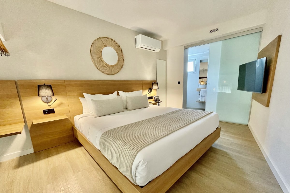 Un dormitorio moderno con una cama de madera, lámparas de noche, un espejo en la pared y una televisión de pantalla plana.