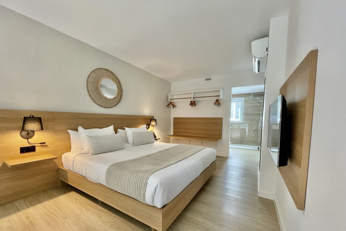 Un dormitorio moderno con una cama de madera, lámparas de noche, un espejo y un televisor montado en la pared.