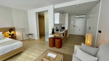 Una habitación de hotel moderna con cama, sofá, pequeña cocina y mesa de comedor.