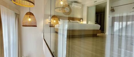 A modern hotel room with a glass partition, a bed, and pendant lights.