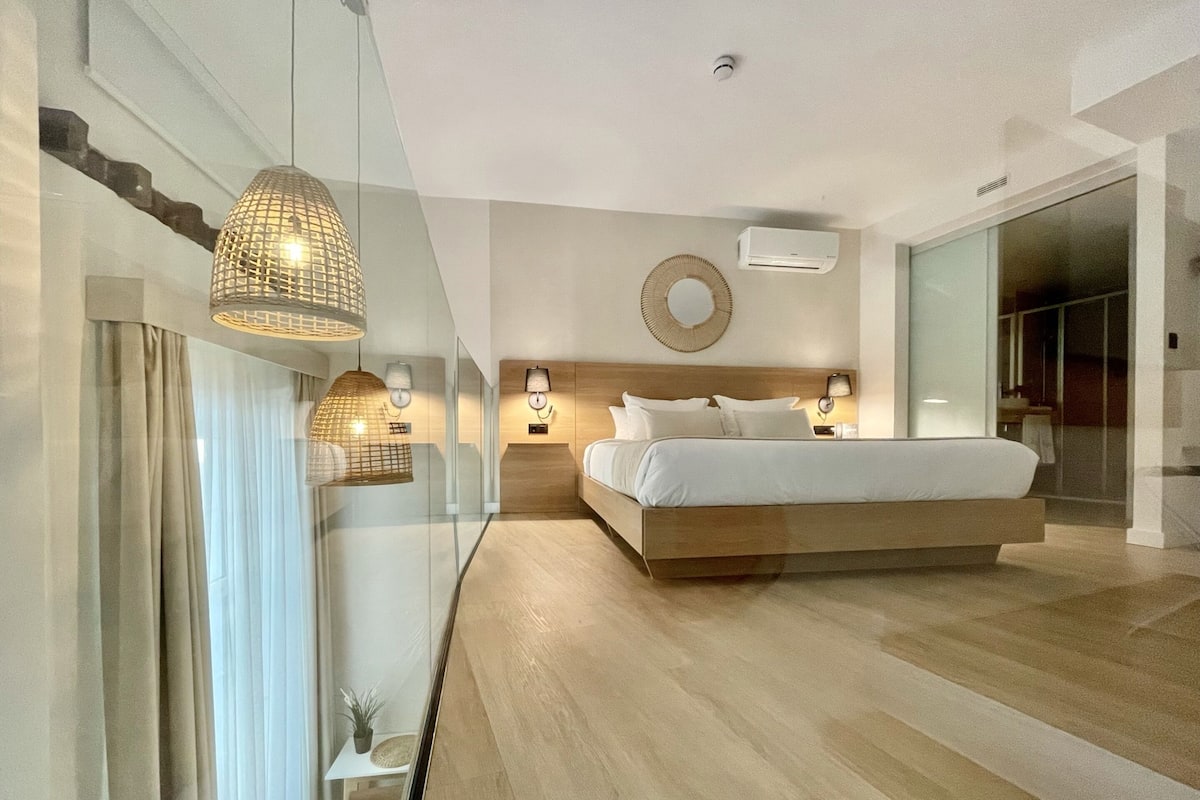 Un dormitorio moderno con una cama grande, lámparas de noche, aire acondicionado instalado en la pared y un separador de vidrio.