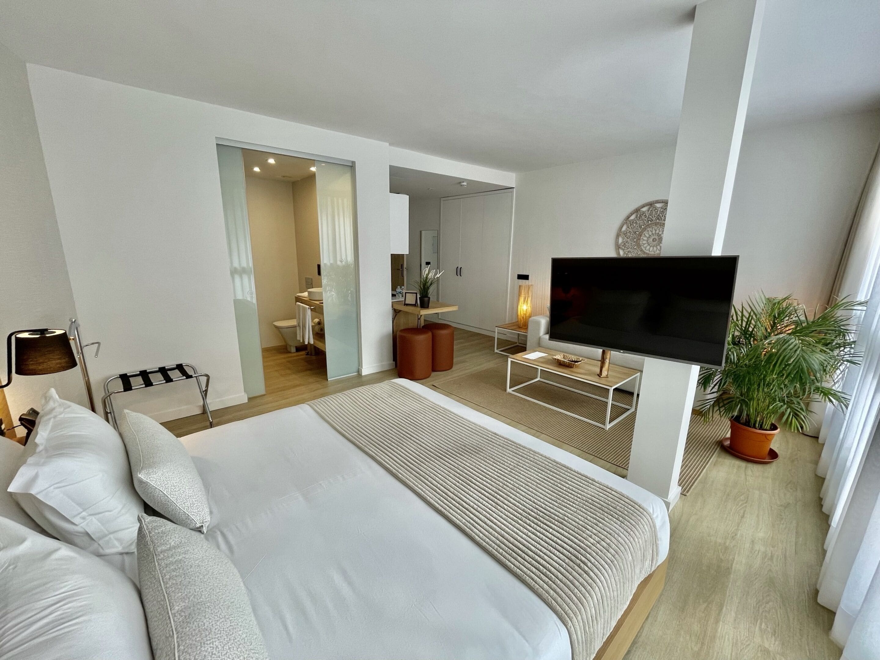 Une chambre d  ’hôtel moderne dotée d’un grand lit, d’un téléviseur à écran plat, d’un petit coin salon et d’une salle de bain visible à travers une porte ouverte.