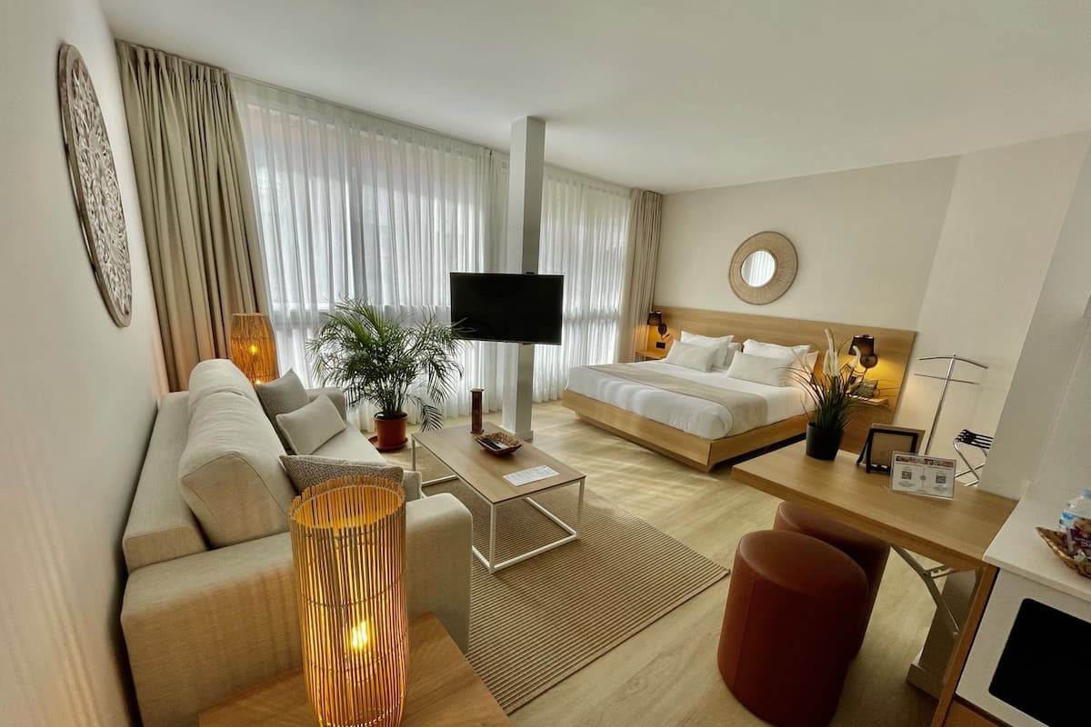 Una habitación de hotel moderna con cama, sofá, escritorio y un ventanal con cortinas.