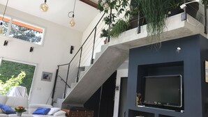 A modern living room with a staircase, a flat-screen TV, and hanging plants. - Architect's villa Lyon Collonges au mont d'or: Swimming pool, Nature, Bocuse, (Collonges-au-Mont-d'Or)