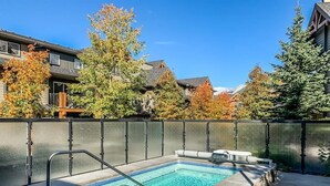 A rectangular outdoor hot tub with a metal ladder, surrounded by a stone wall and a metal fence. - Canmore 2BR Condo, Near Banff (Dead Mans Flats)