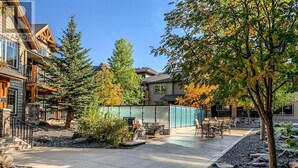A residential area with a paved patio, outdoor seating, and a large tree. - Canmore 2BR Condo, Near Banff (Dead Mans Flats)