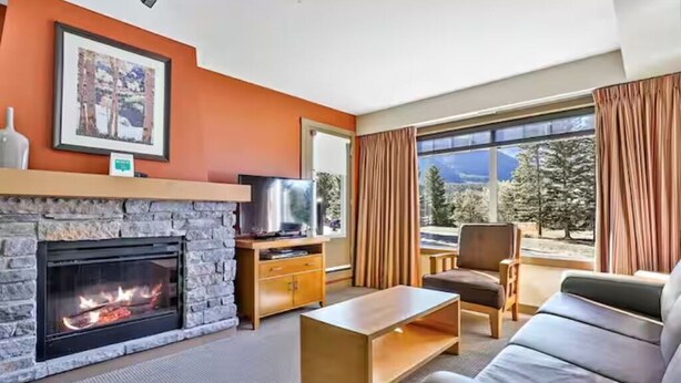 A living room with a fireplace, a sofa, a coffee table, and a television. - Canmore 2BR Condo, Near Banff (Dead Mans Flats)
