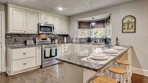 A kitchen with white cabinets, granite countertops, a central island with stools, and a microwave.