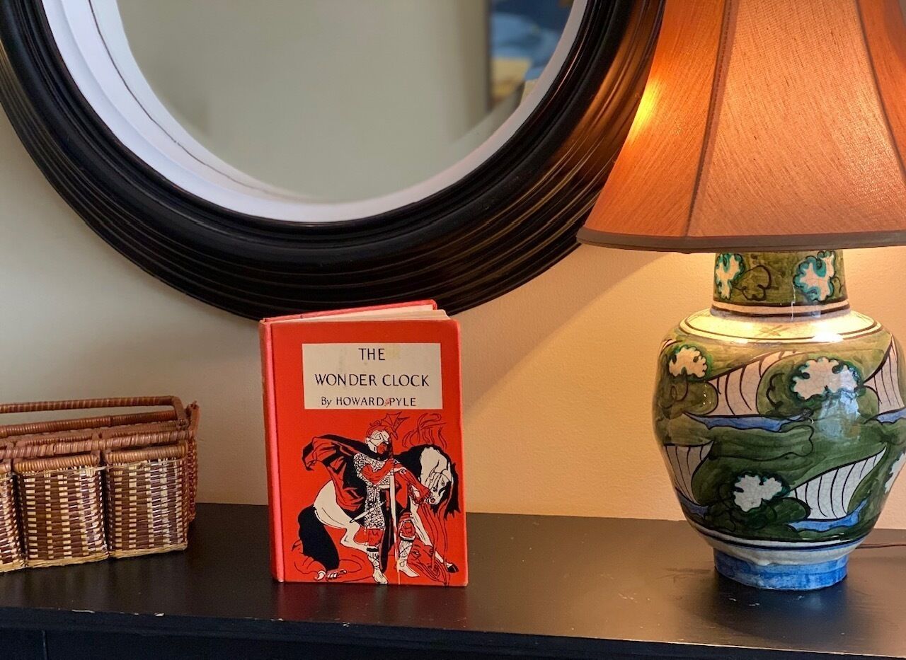 Un livre intitulé « The Wonder Clock » de Howard Pyle, posé sur une table à côté d’un vase décoratif.