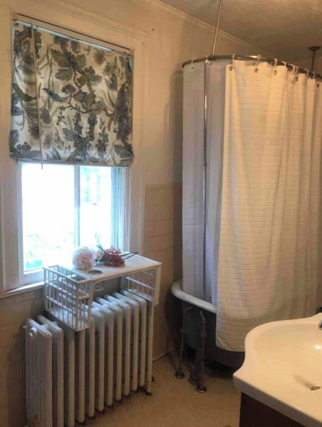 Un baño con un radiador, una ventana con cortinas florales y una zona de ducha.