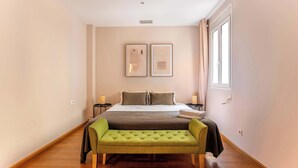 A bedroom with a bed, bedside tables, a bench, and two framed pictures on the wall. - Elegant and historic 3BD in Pl Urquinaona! (Barcelona)