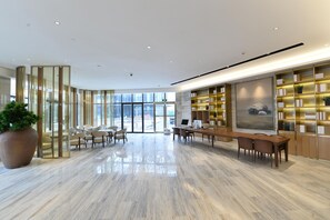Un hall d’hôtel moderne avec un sol en marbre, un espace salon et une bibliothèque contenant des livres et des objets décoratifs.