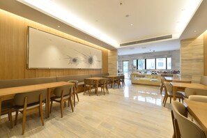 Un comedor moderno con mesas y sillas de madera, un cuadro abstracto grande en la pared y vistas al exterior a través de amplias ventanas.