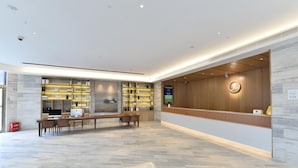 A modern reception area with a wooden reception desk, a seating area with tables and chairs, and a wall with shelves displaying items. - Ji Hotel (Shanghai)