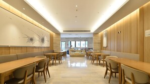 A modern dining area with wooden tables and chairs, a marble floor, and a large wall art piece. - Ji Hotel (Shanghai)