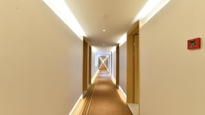 A hotel corridor with a carpeted floor, wooden doors, and a red emergency exit sign. - Ji Hotel (Shanghai)
