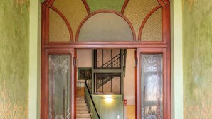 An entrance with a green and yellow wall, a wooden door with glass panels, and a staircase leading to an upper floor.
