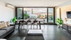 A modern living room with a dining area, large sliding glass doors leading to a balcony, and a TV on the right.