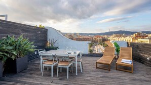 A rooftop terrace with a dining table and chairs, two lounge chairs, and potted plants.