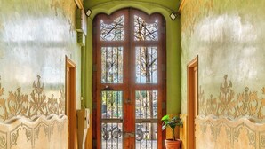 A hallway with a green wall, a wooden door with glass panels, and a potted plant.