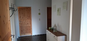 Un couloir avec une porte en bois, une armoire blanche ornée d’une lanterne et des œuvres d’art accrochées au mur.