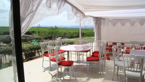 A covered outdoor dining area with white tables and chairs, red cushions, and a view of a green landscape. - Come all, for an exceptional stay. (Tahla)