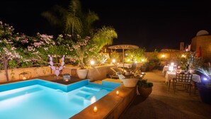 An outdoor swimming pool with a sunken seating area, surrounded by potted plants and outdoor furniture. - RIAD HIZAD (Marrakech)