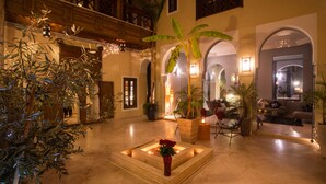 A spacious lobby with a central fire feature, seating area, and decorative plants. - RIAD HIZAD (Marrakech)