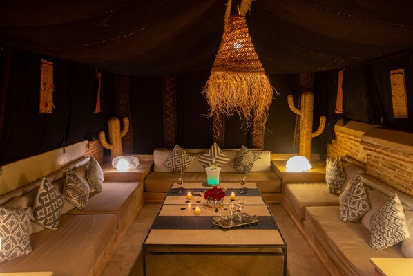 A cozy lounge area with a central table, cushioned seating, and decorative elements like cacti and a hanging light fixture. - RIAD HIZAD (Marrakech)